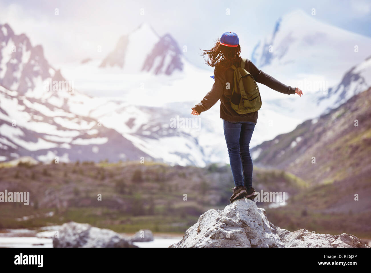 Girl stands on big rock and looks at snow capped mountains. Travel, backpacker or tourism concept Stock Photo