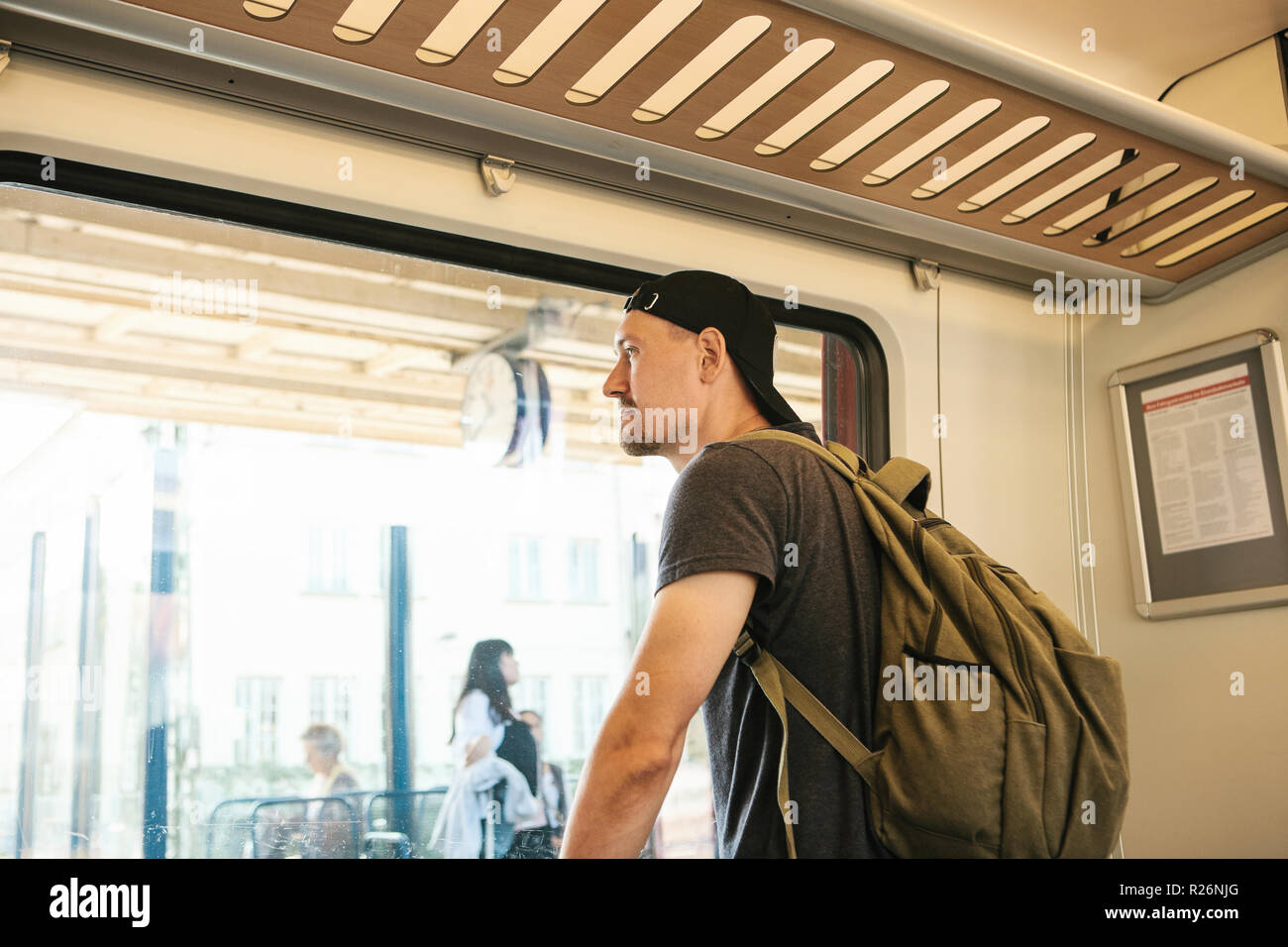 A young guy with a backpack inside the train looks out the window at ...