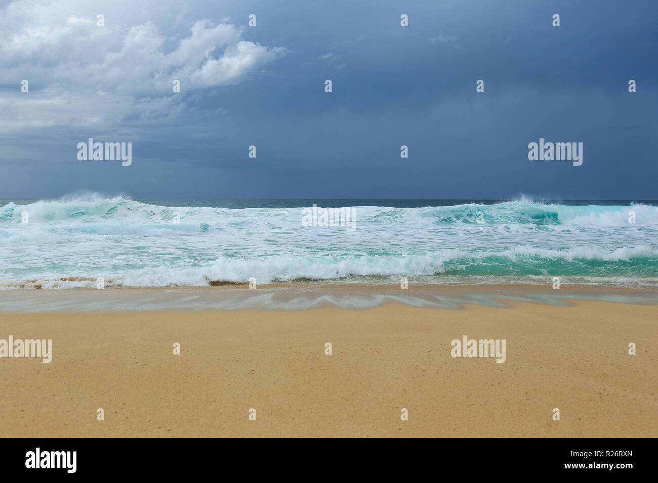 Seascape with large ocean waves washing over sandy beach with dark grey sky above. Stock Photo