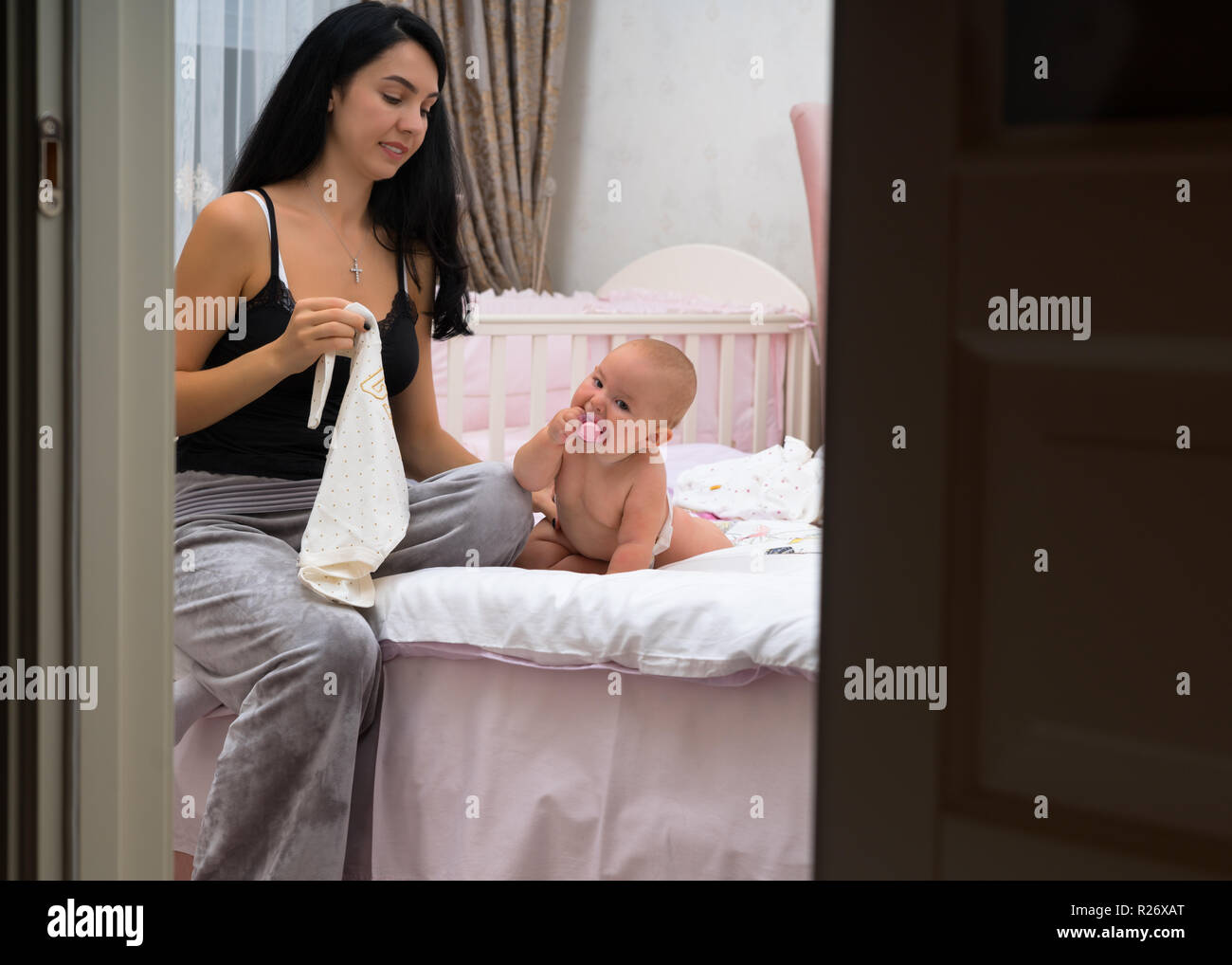 Young Mother Changing The Nappy Of Her Baby Daughter In A Nursery