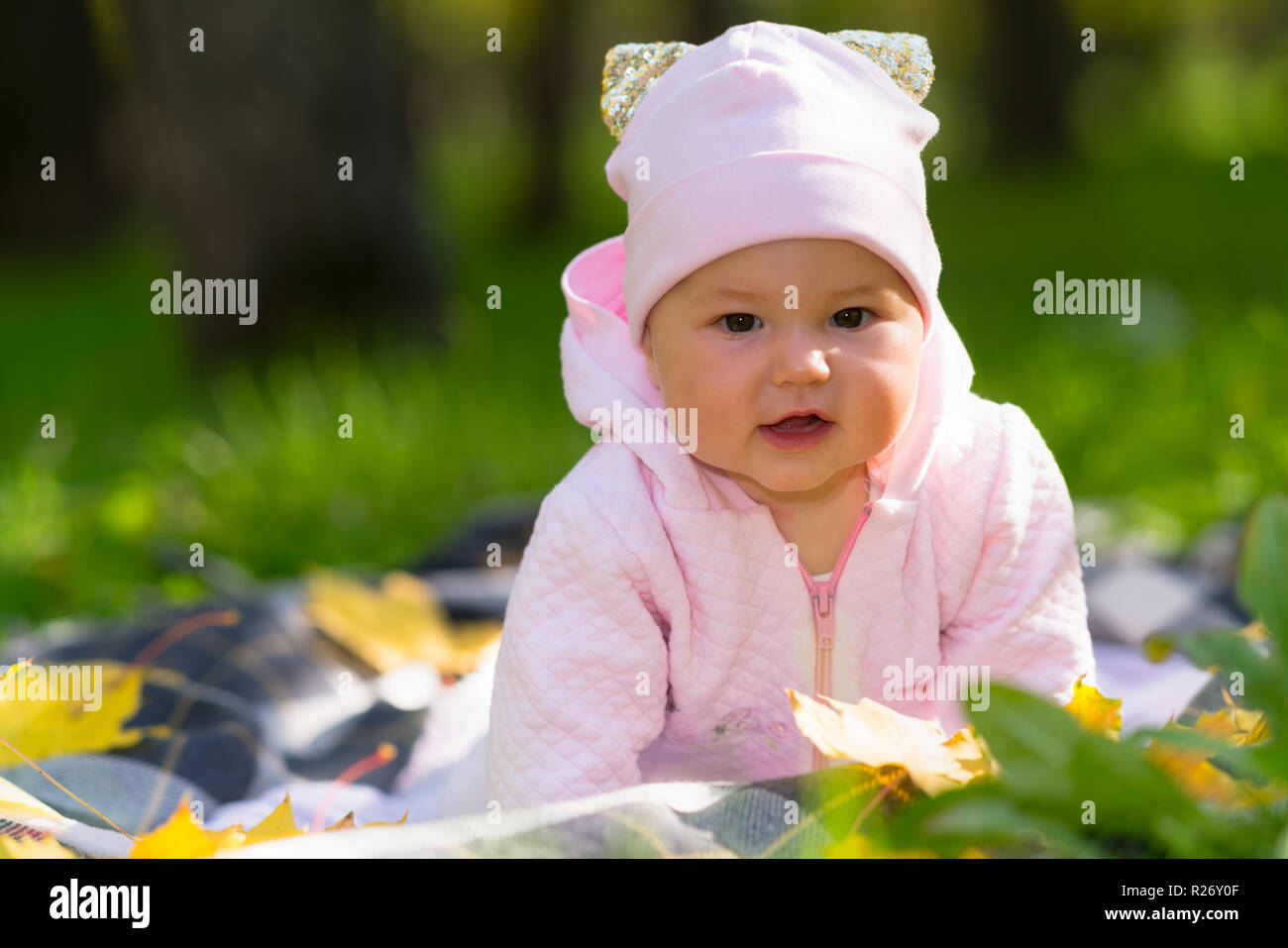 Curious little baby girl watching the camera raising herself up on her arms  as she crawls over a blanket on the brass in an autumn park Stock Photo -  Alamy