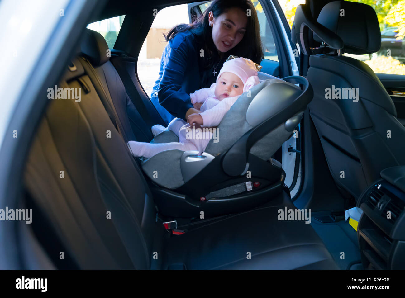 Mother putting her baby in baby chair on the backseat of the car, viewed from the other side of the vehicle Stock Photo
