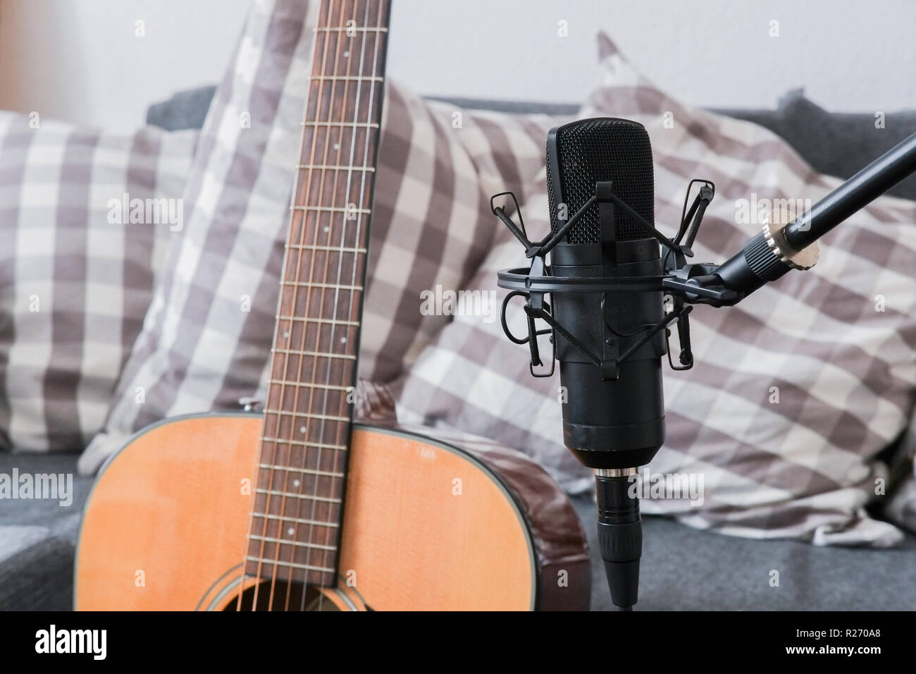 Condenser microphone on a stand with acoustic guitar in the background