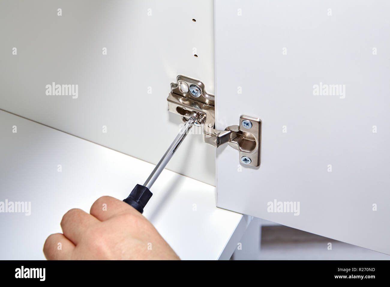 The furniture assembler adjusts the mechanism for opening the door of