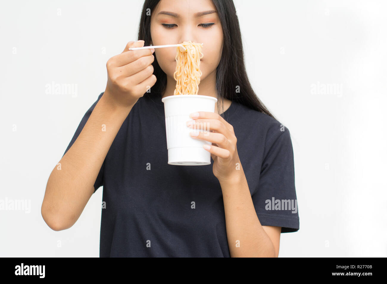 Young beautiful asian woman eating yummy hot and spicy instant noodle using chopsticks isolated on gray background.Unhealthy concept Stock Photo