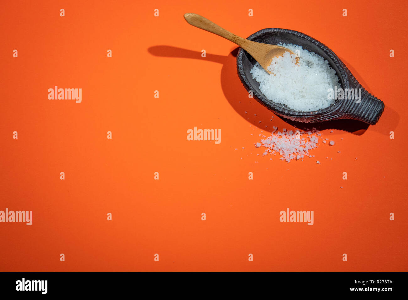 coarse salt in small decorative bowl with wooden spoon on orange background Stock Photo