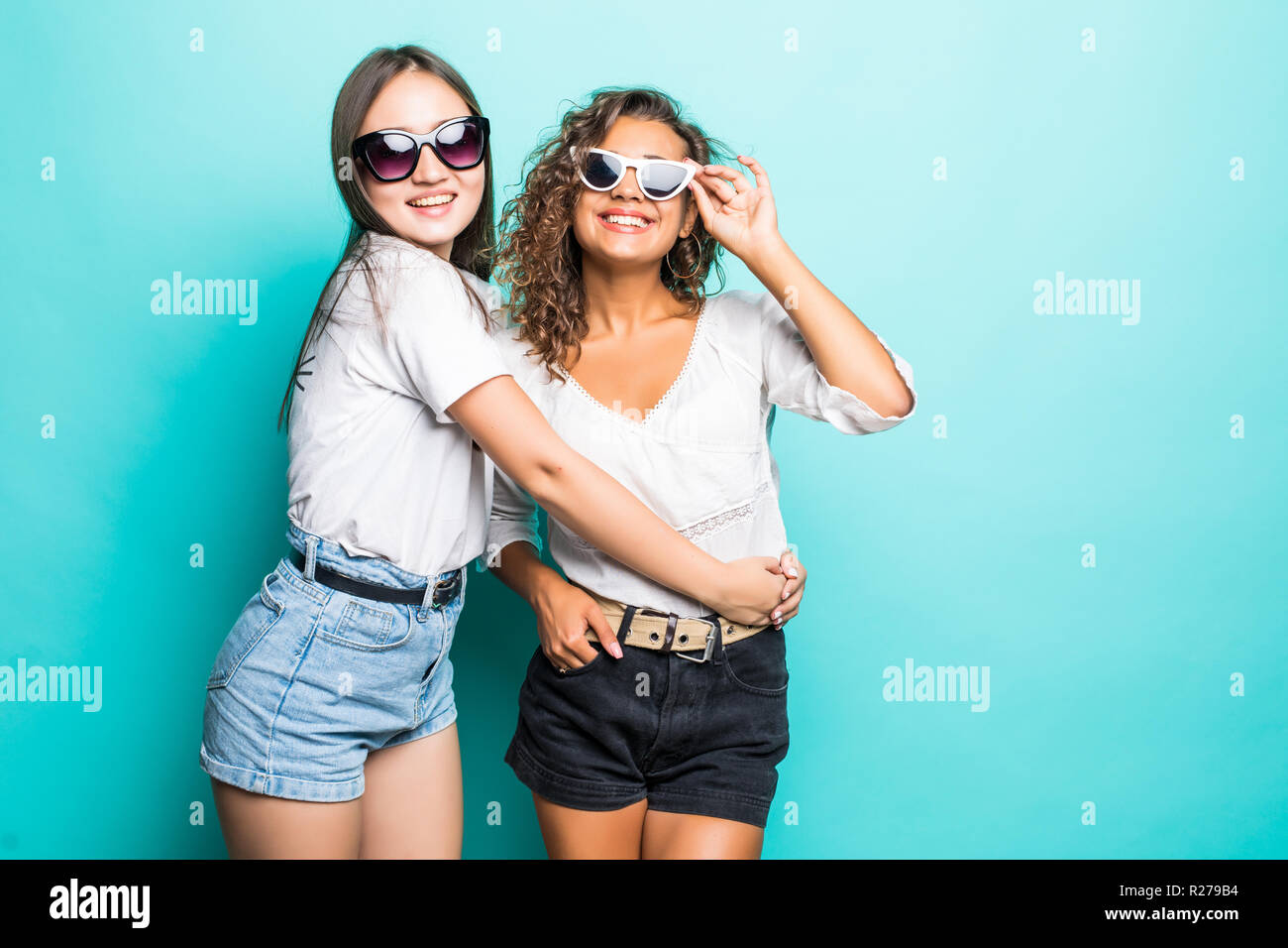 Friends forever. Two cute lovely girl friends in sunglasses posing with  smile on blue background Stock Photo - Alamy