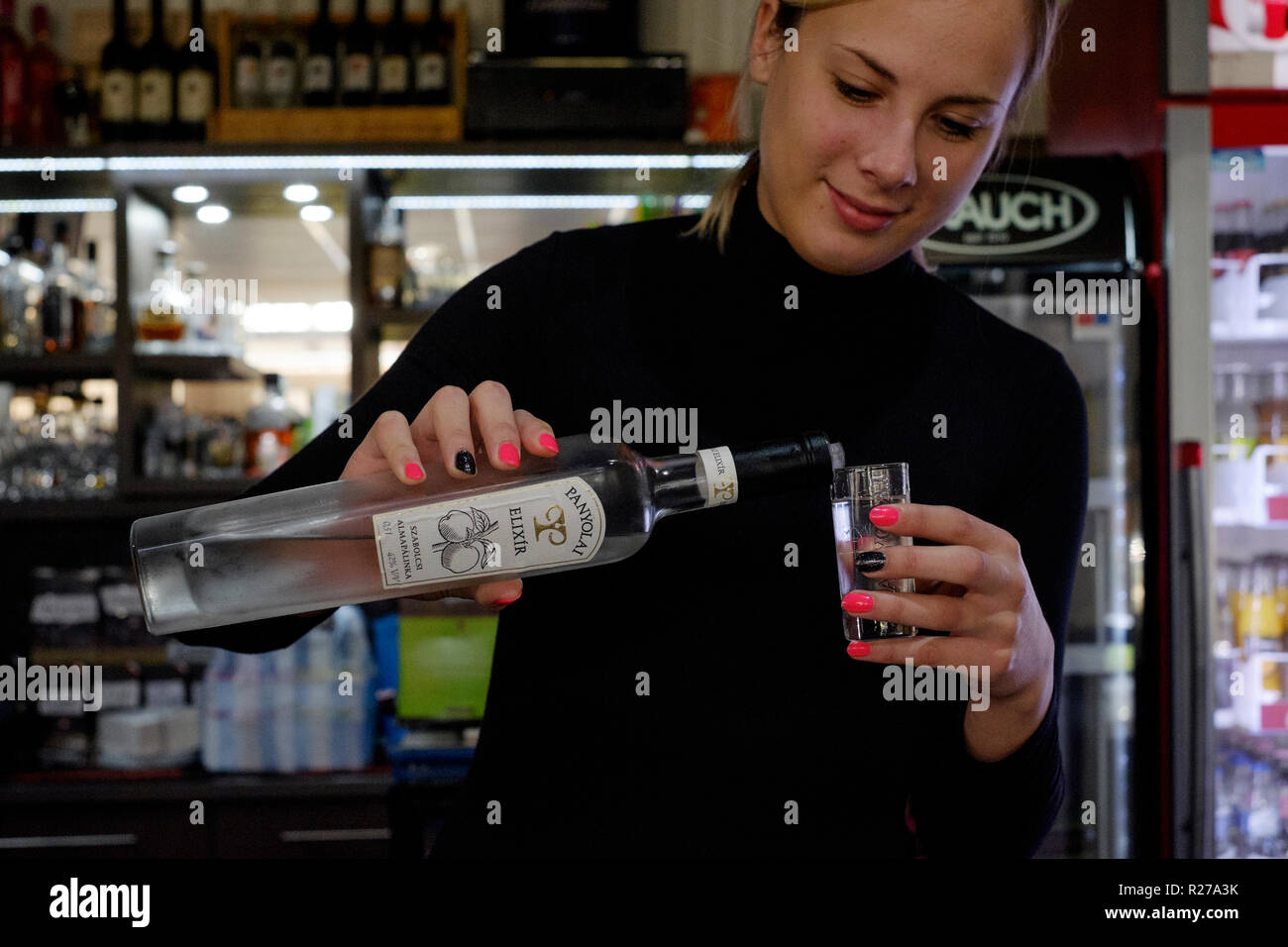 young pretty female barmaid pouring from a bottle of traditional
