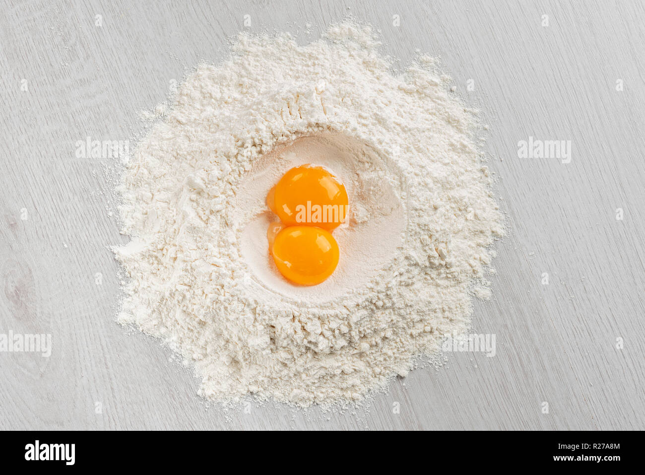 pile of flour with egg yolks for dough on table, top view. Stock Photo