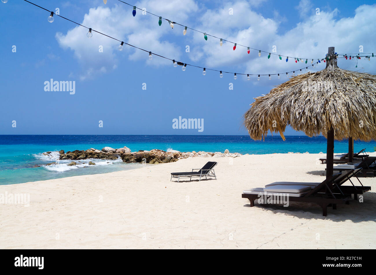 Tiki hut on the beach with white sand, blue water and colorful lights. Paradise on Curacao. Stock Photo