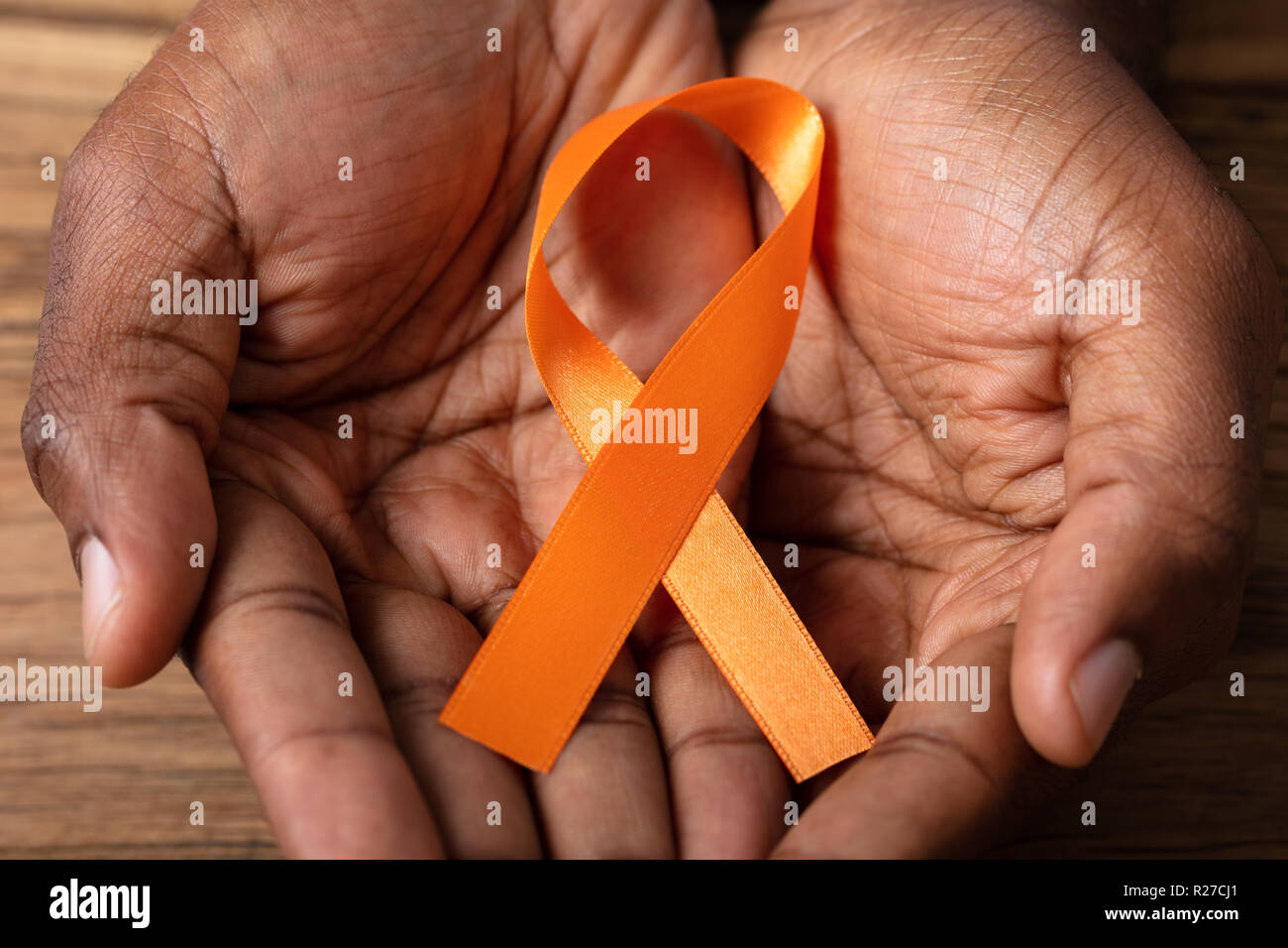 Person's Hand Holding Ribbon To Support Kidney Cancer And Leukemia Awareness Stock Photo