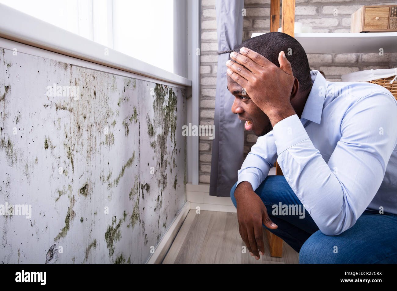 Side View Of A Shocked Young African Man Looking At Mold On Wall Stock Photo