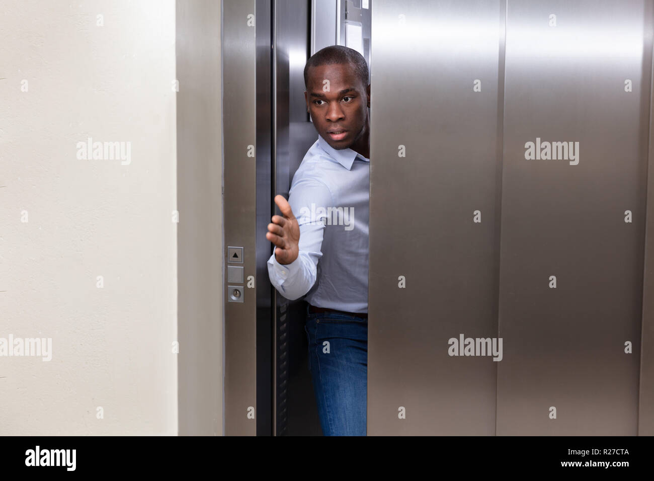 Young African Man Trying To Stop Elevator Door With His Hand Stock Photo
