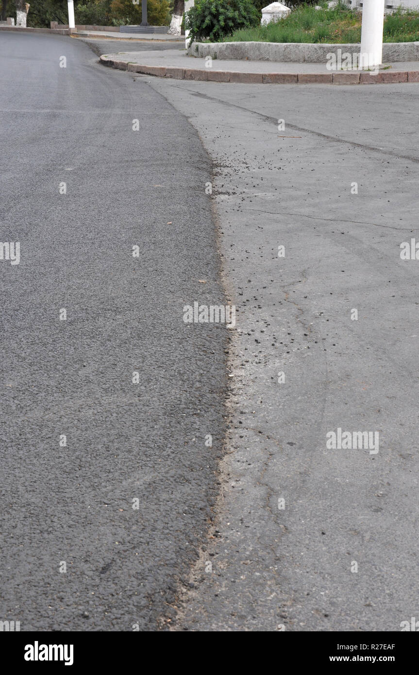 Partly repaired roadway with a vertical edge between the newly laid asphalt concrete on the left and the older area on the right. Stock Photo