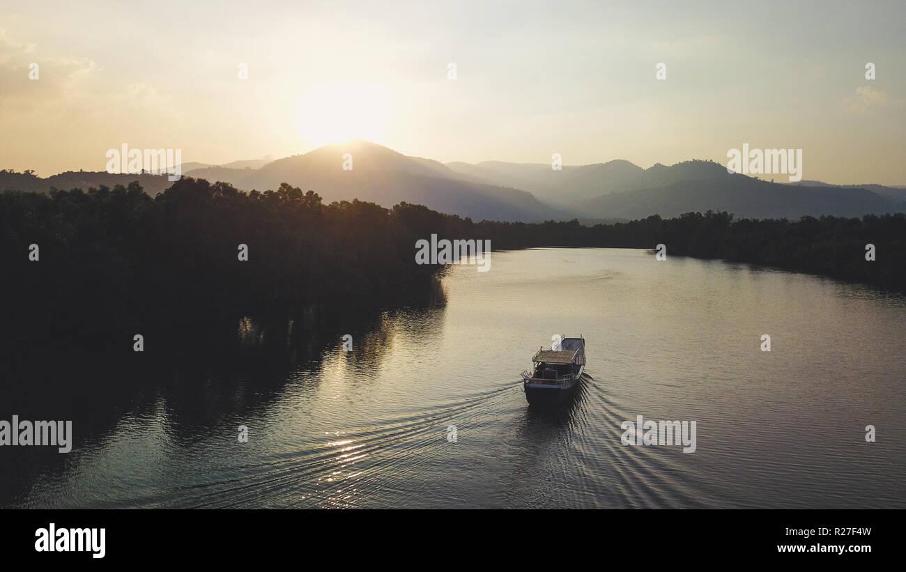 Boat sailing towards Sunset in front of Mountain Ridge. Drone Shot. Stock Photo