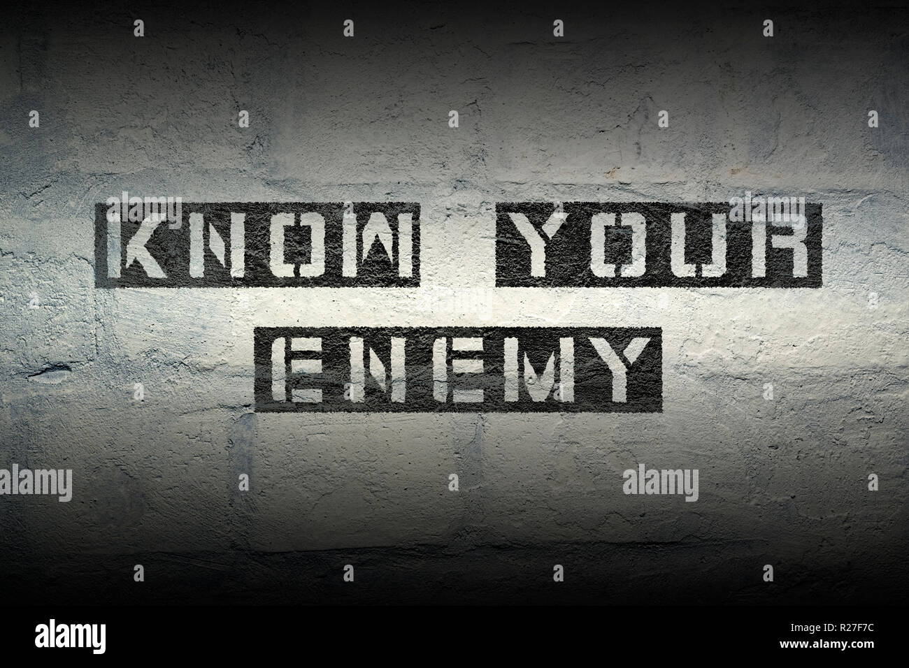 know your enemy stencil print on the grunge white brick wall Stock Photo