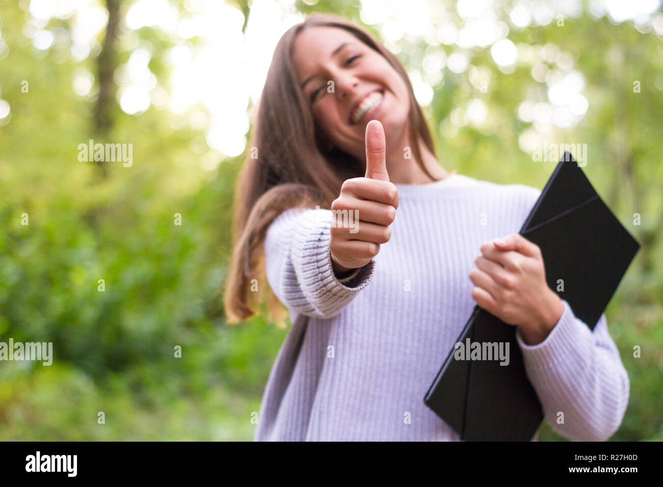 Female or young Caucasian european college girl or student with folder in college after doing final exam and refresher classes with thumps up smile an Stock Photo