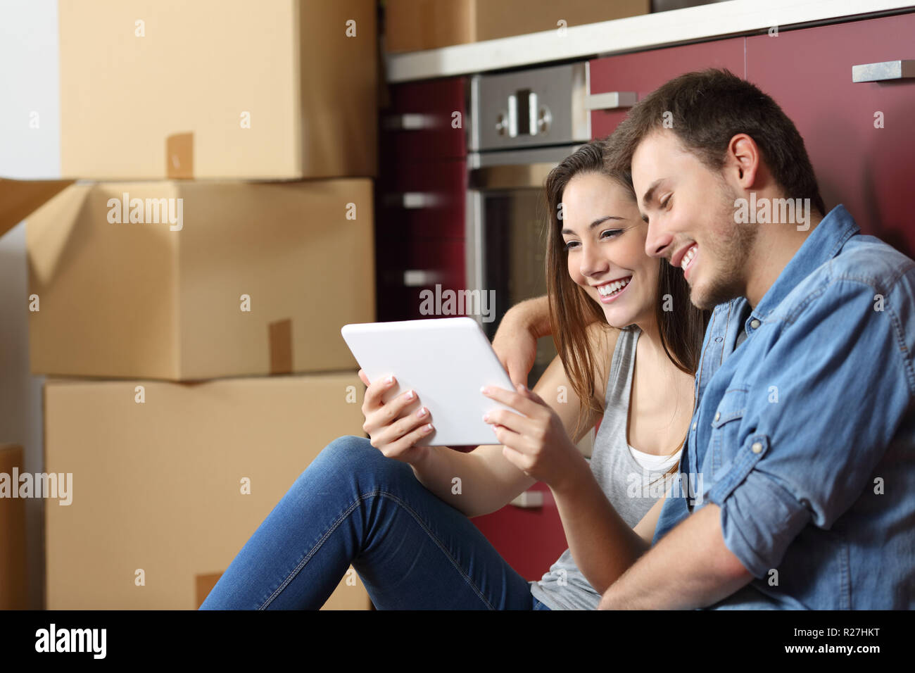 Couple sitting on the floor of the kitchen and buying online with a tablet and moving home Stock Photo