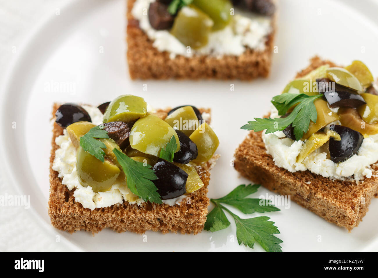 Rye bread toast (canape) with black and green olives, feta cheese and  parsley. Tasty snack for gourmets. Selective focus Stock Photo - Alamy