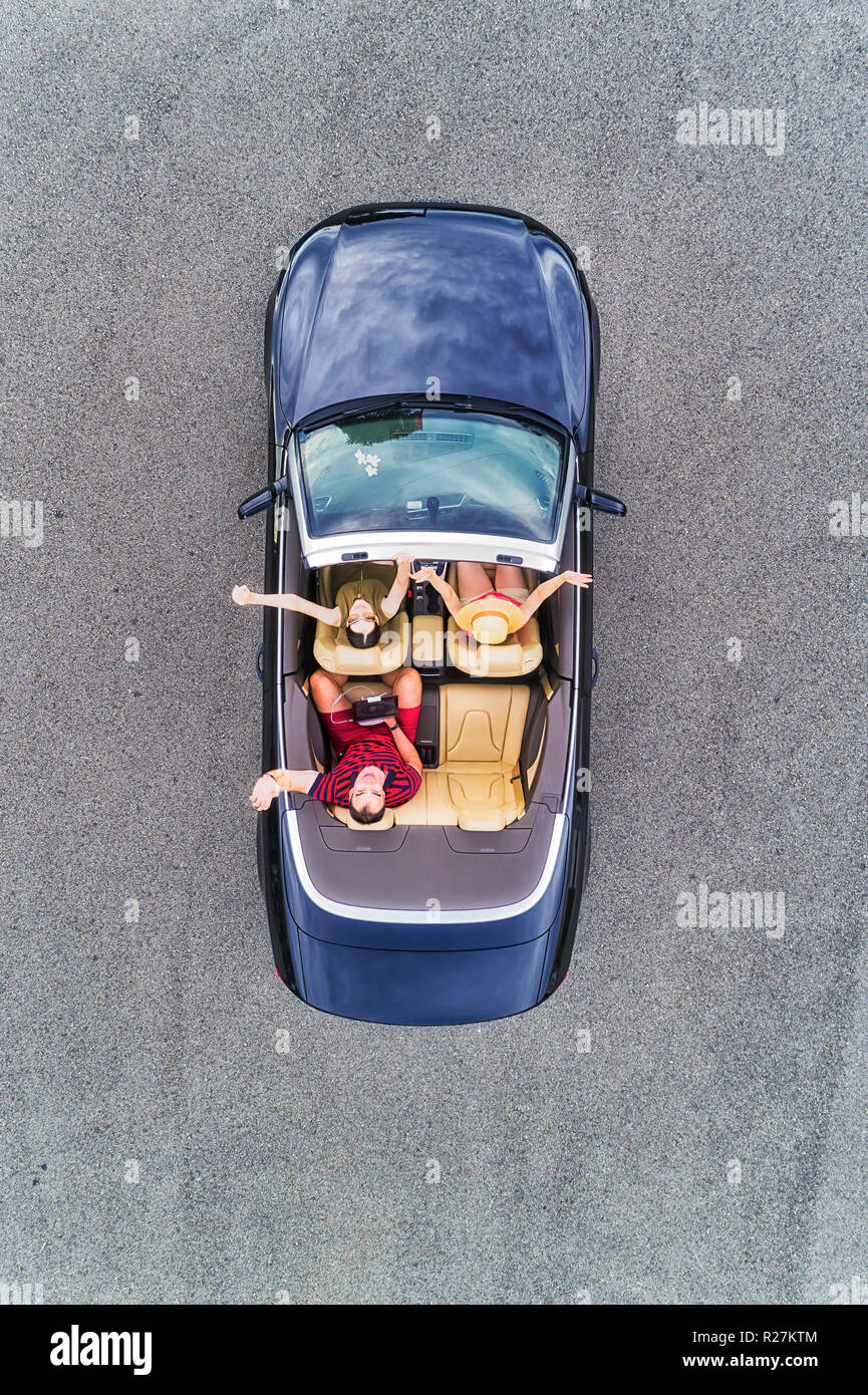 Small passenger sports convertible car with soft top down and happy family of young people enjoying lifestyle and freedom in aerial top down view. Stock Photo