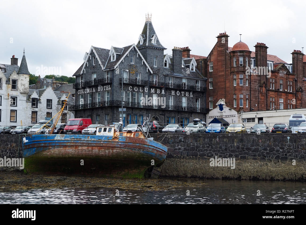 Oban, United Kingdom - February 20, 2010: shipwreck and city architecture along sea quay. Bay with houses on grey sky. Resort town with hotels. Summer vacation on island. Travelling and wanderlust. Stock Photo
