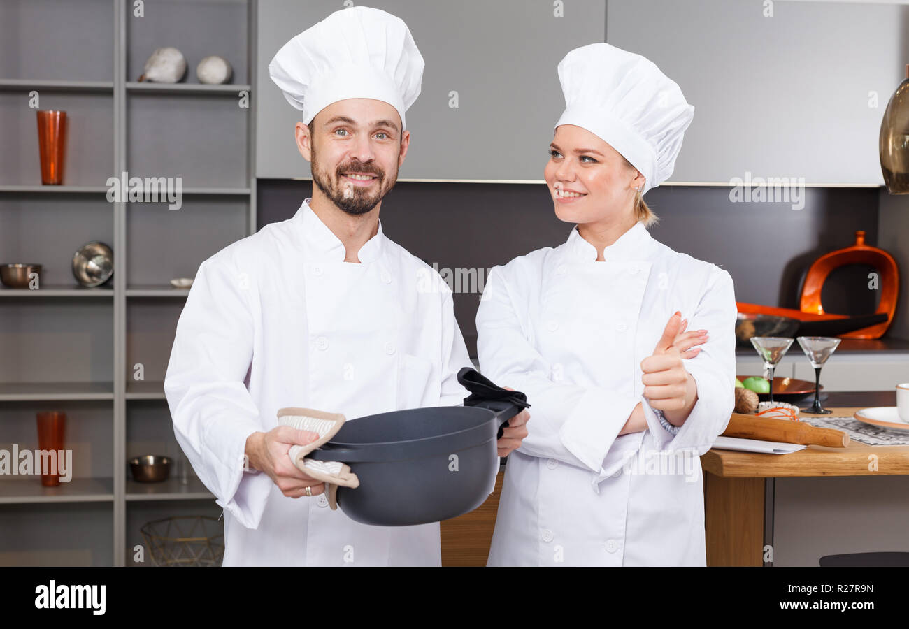 Two confident personal chefs in white coats standing in modern interior of private kitchen Stock Photo