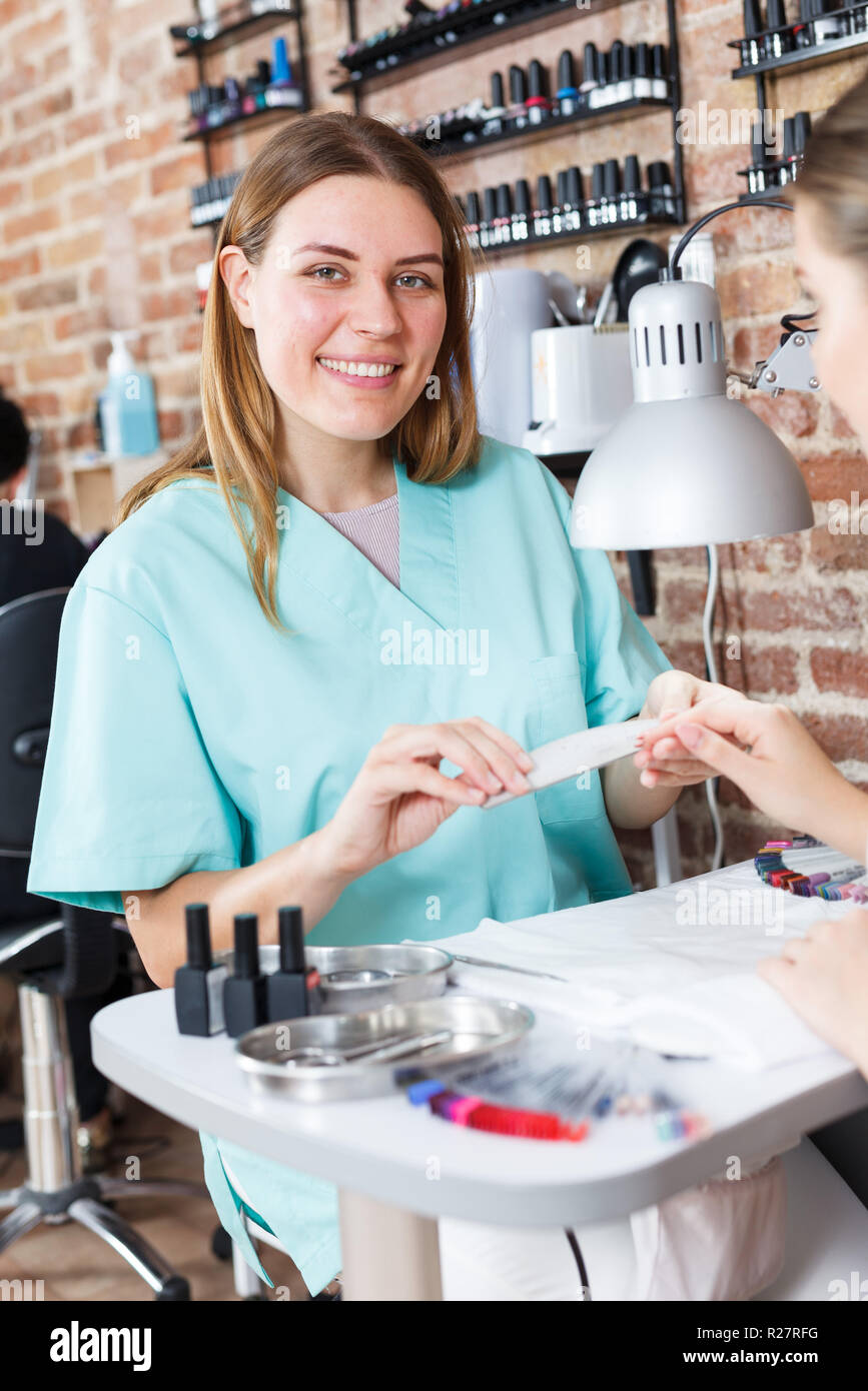 Professional manicurist filing and shaping nails to girl in modern ...