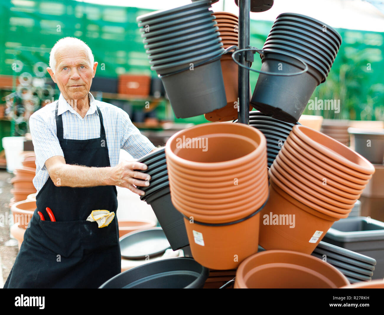 Senior owner of greenhouse choosing pots for plants in garden material