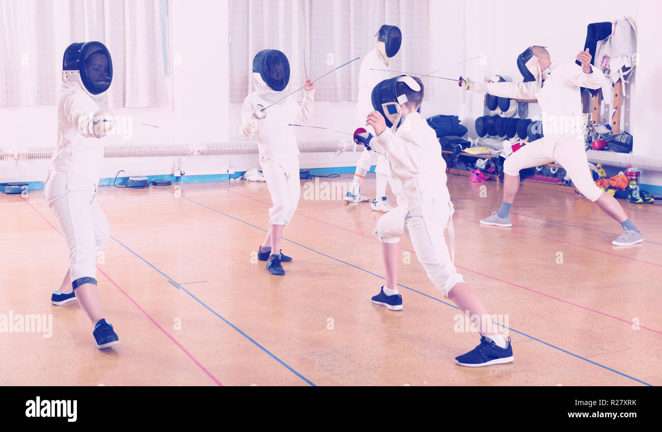 Mixed age group of athletes at fencing coach, training attack movements
