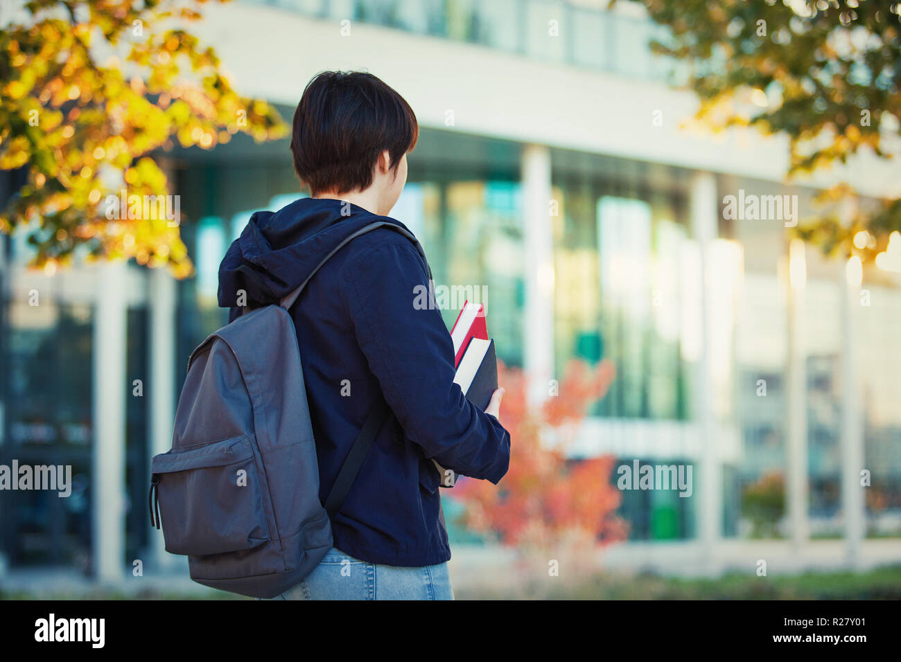 Rear view student girl portrait carrying backpack and books. Autumn lifestyle concept. Stock Photo