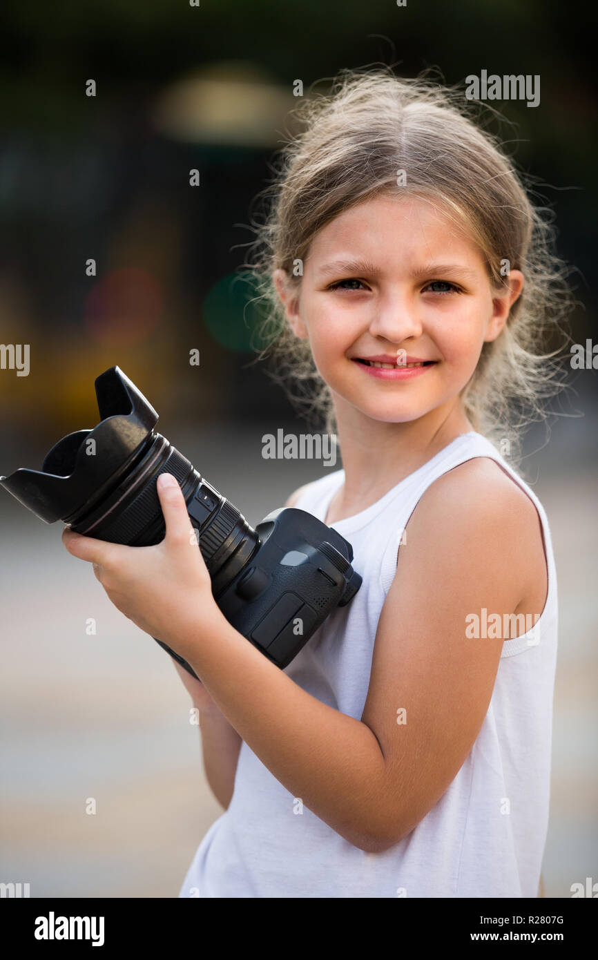 smiling girl  8-10 years old in elementary school age holding photo camera in hands outdoors Stock Photo