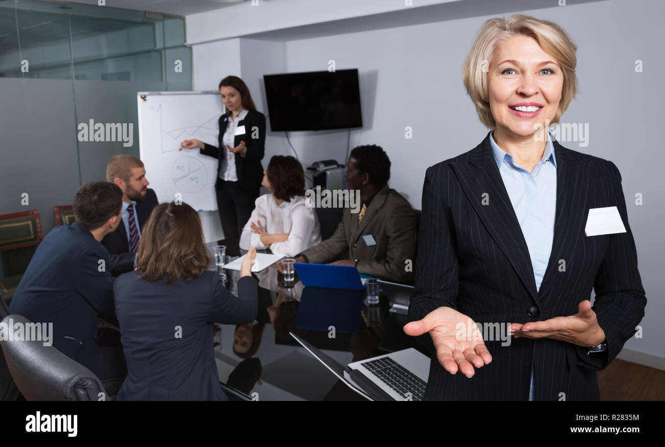 Smiling elegant adult woman with multinational business team behind during joint work Stock Photo
