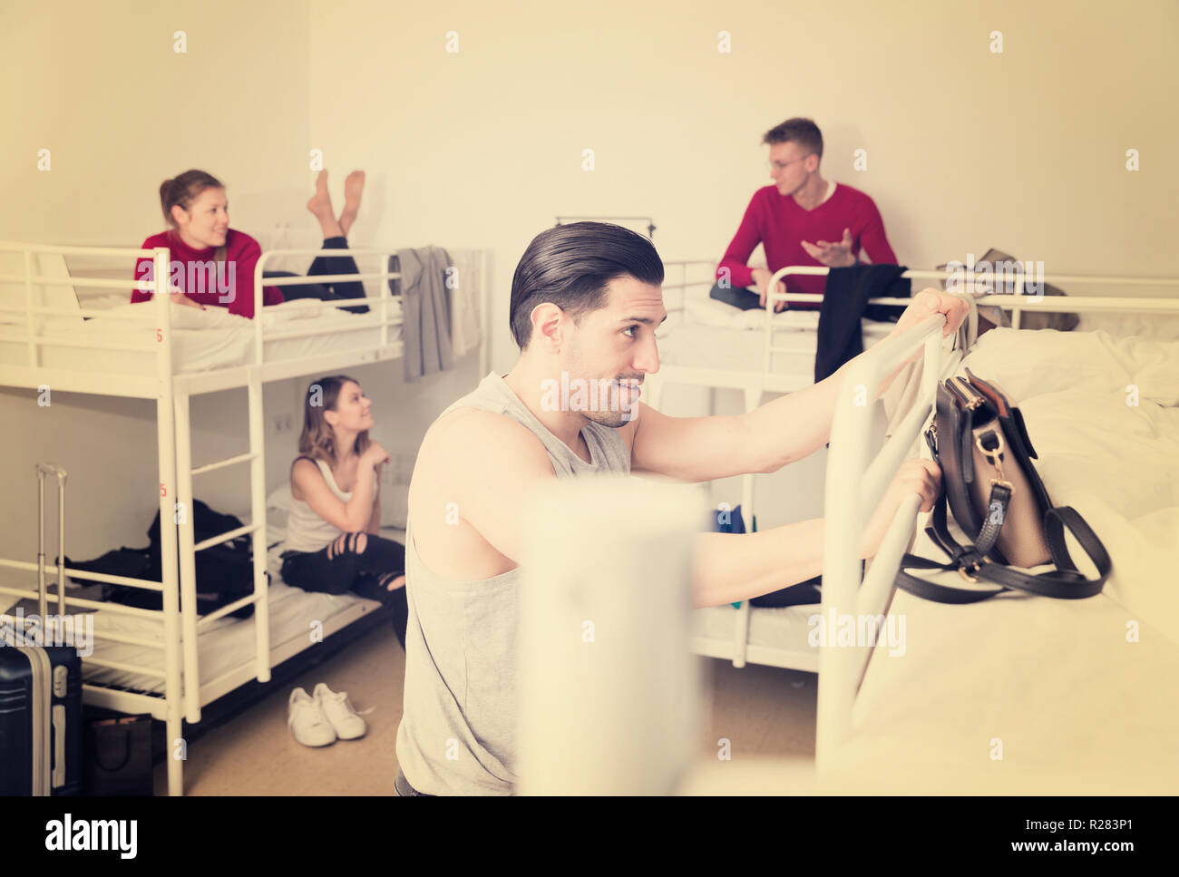 Man traveler staying in hostel, getting up to top bunk of twostory bed