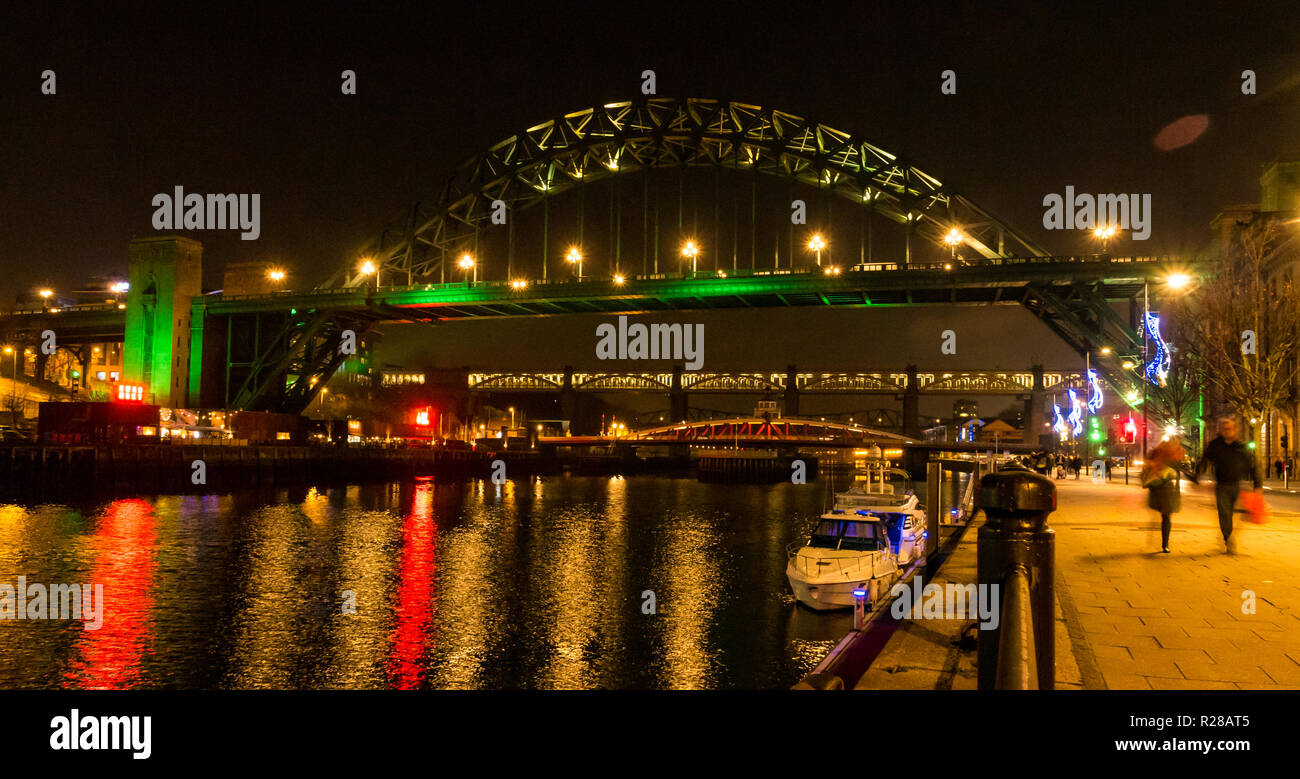 Newcastle Upon Tyne, England, United Kingdom, 17th November 2018. View from The Quayside with people walking along the River Tyne and bridges lit up at night including the High Level Bridge, the Swing bridge and the Tyne Bridge with reflections in the water Stock Photo