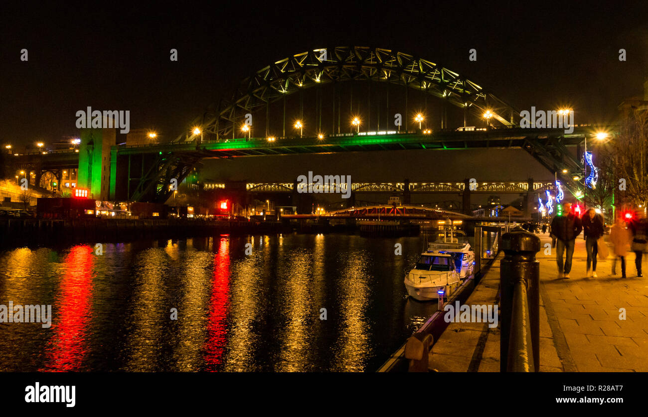 Newcastle Upon Tyne, England, United Kingdom, 17th November 2018. View from The Quayside with people walking along the River Tyne and bridges lit up at night including the High Level Bridge, the Swing bridge and the Tyne Bridge with reflections in the water Stock Photo