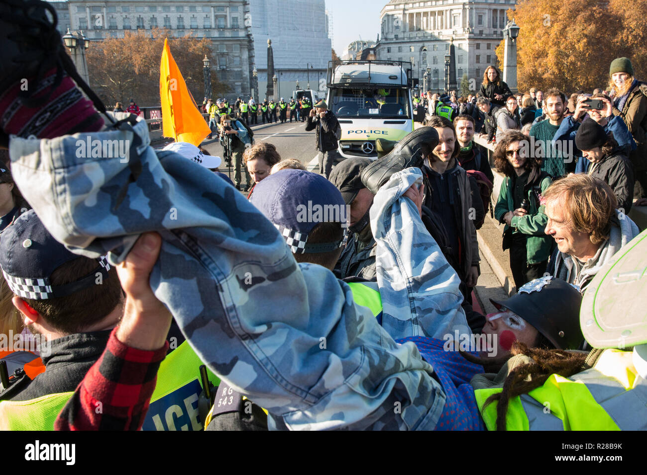 London, UK. 17th November, 2018. Police officers arrest a man after environmental campaigners from Extinction Rebellion blocked Lambeth Bridge, one of five bridges blocked in central London, as part of a Rebellion Day event to highlight 'criminal inaction in the face of climate change catastrophe and ecological collapse' by the UK Government as part of a programme of civil disobedience during which scores of campaigners have been arrested. Clowns from Clandestine Insurgent Rebel Clown Army (CIRCA follow them. Credit: Mark Kerrison/Alamy Live News Stock Photo