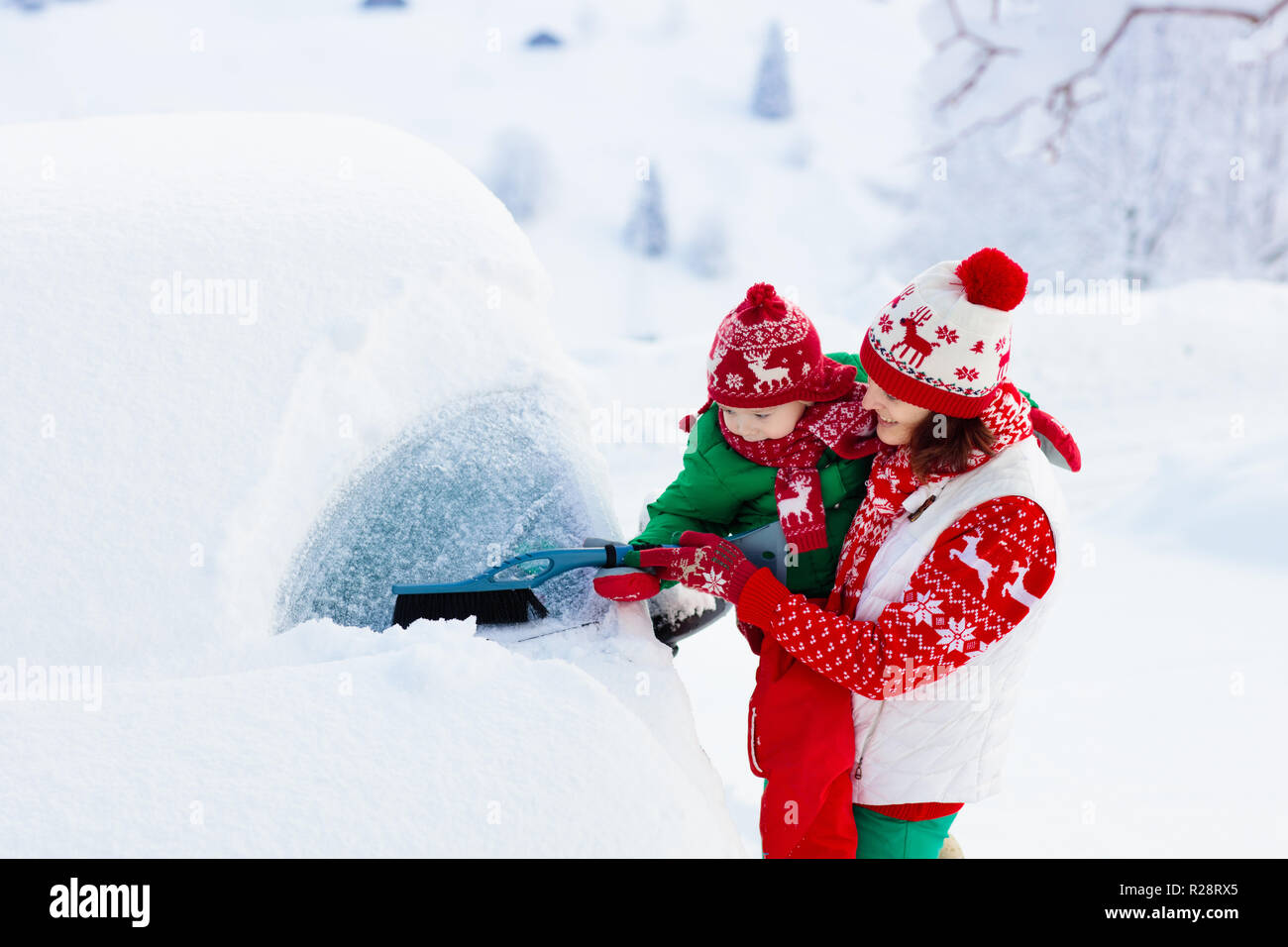 Mother and child brushing and shoveling snow off car after storm