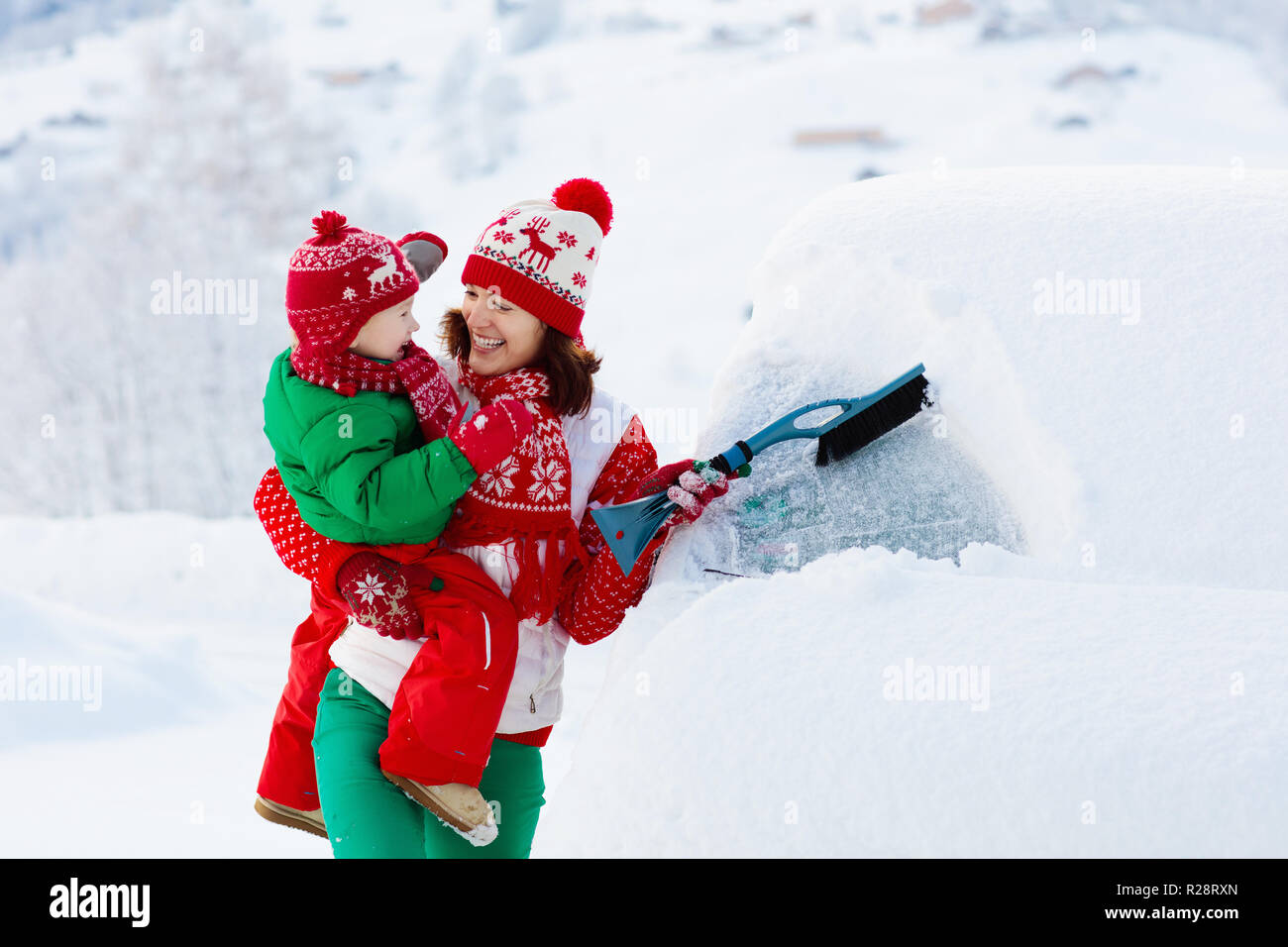 Mother and child brushing and shoveling snow off car after storm