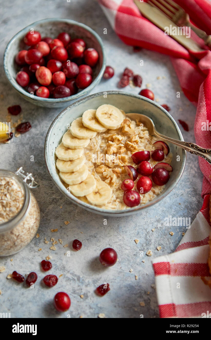 Ceramic bowl of oatmeal porridge with banana, fresh cranberries and