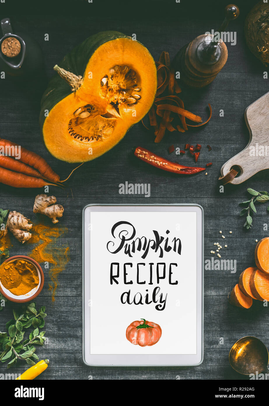 Tablet pc with text lettering: Pumpkin recipe daily. Orange cooking ingredients: sweet potato, carrots, turmeric powder,chili and ginger for tasty cui Stock Photo