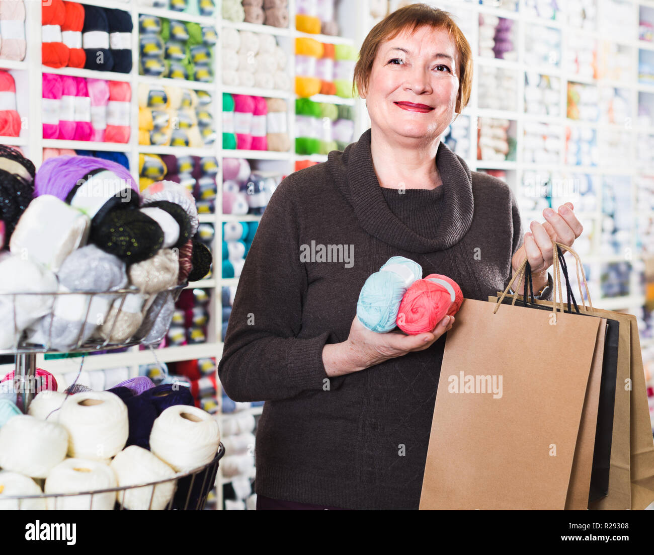 Mature female is standing in needlework store with shopping bags Stock