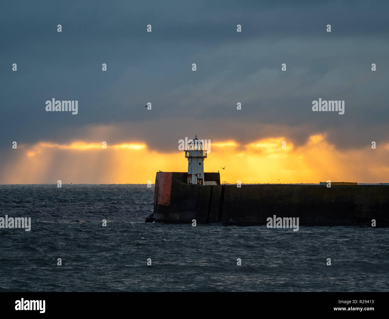 Sunrise behind a small lighthouse at the breakwater of Aberdeen harbour. Stock Photo