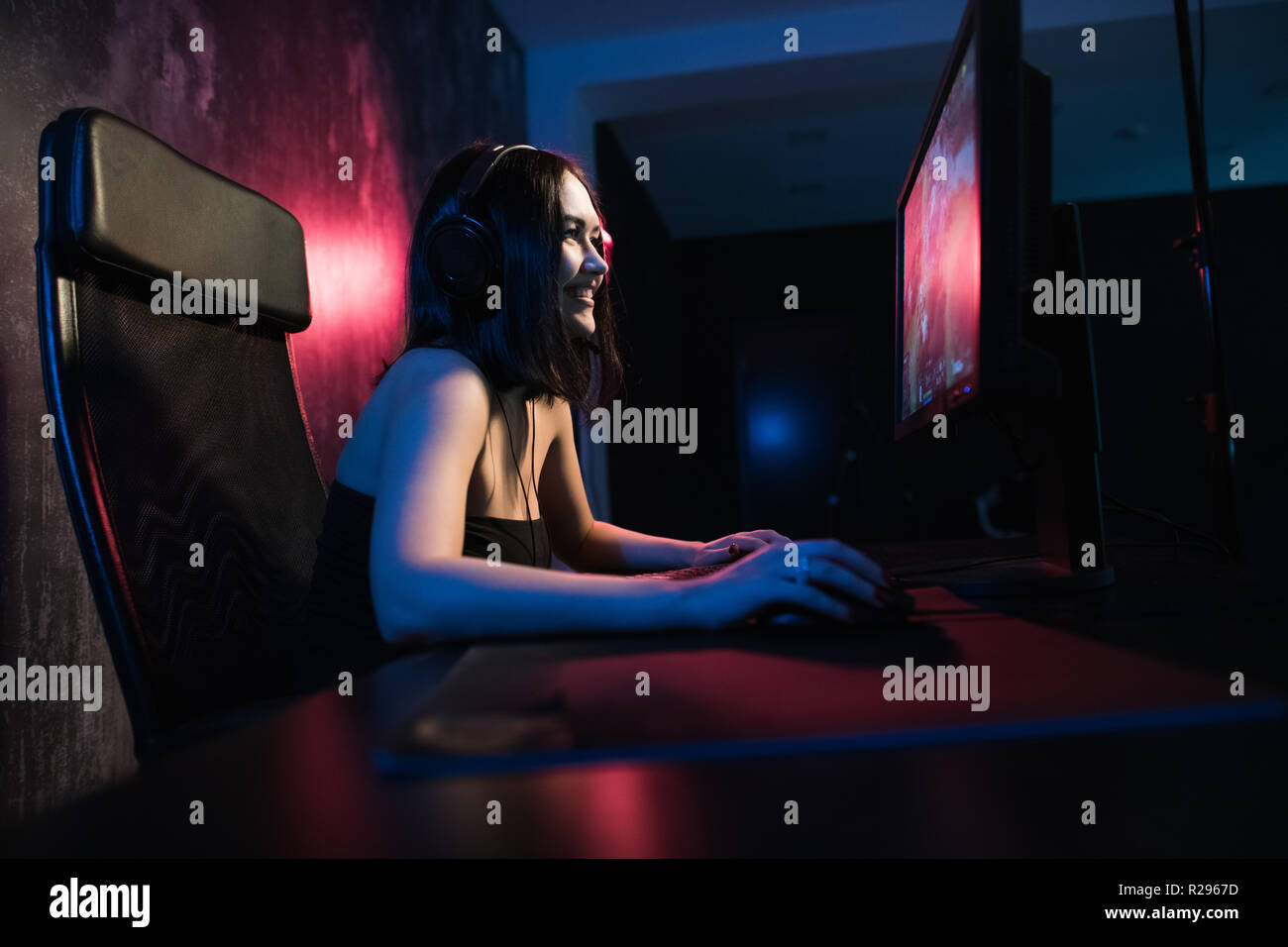 A cute female gamer girl sits in a cozy room behind a computer and ...
