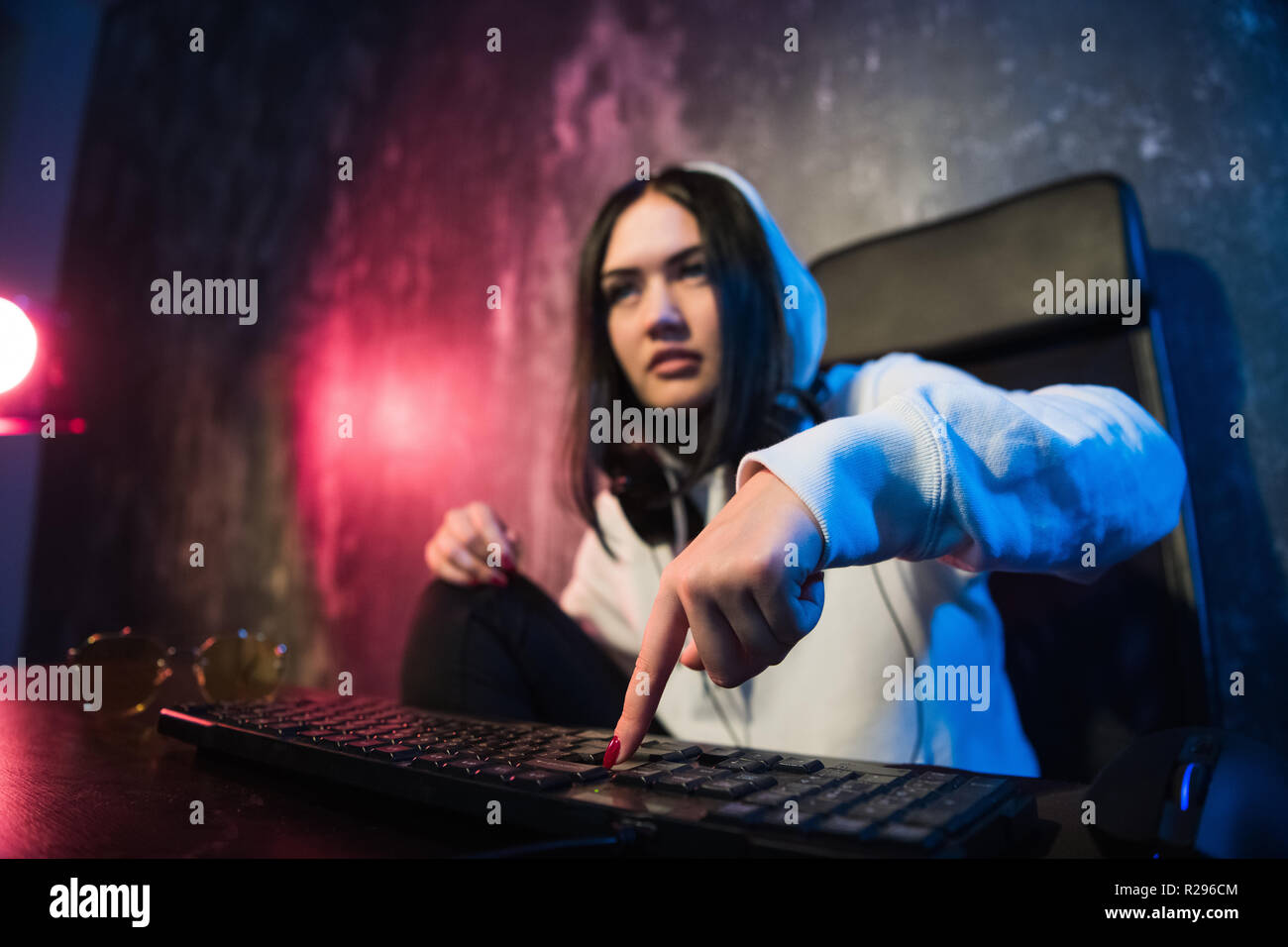 Woman in the hood sitting and working at laptop as hacker. Running malware program on computer in the internet with malevolent smile on her face Stock Photo