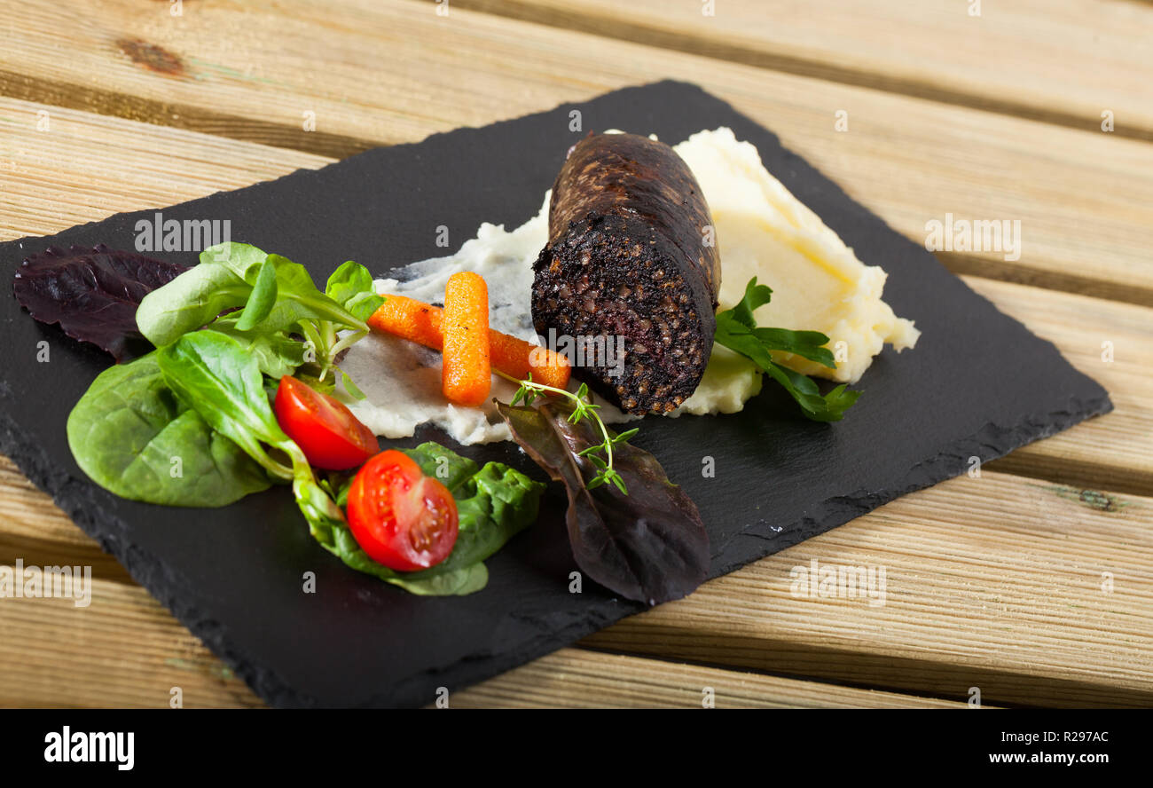 Black pudding sausage served with potato puree, vegetables and greens on slate Stock Photo