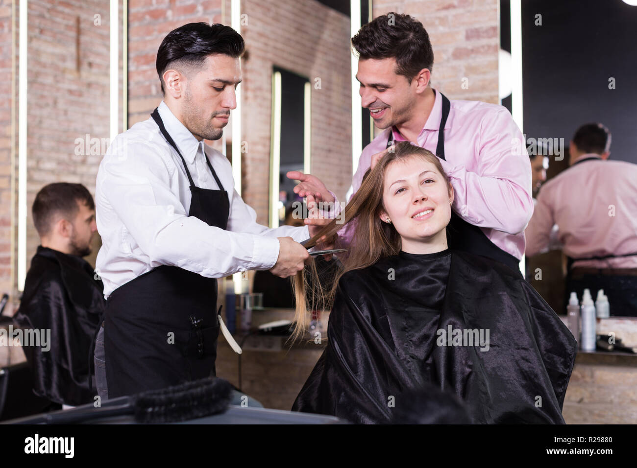 Two Skilled Men Hairdressers Making Hairstyle For Young Female