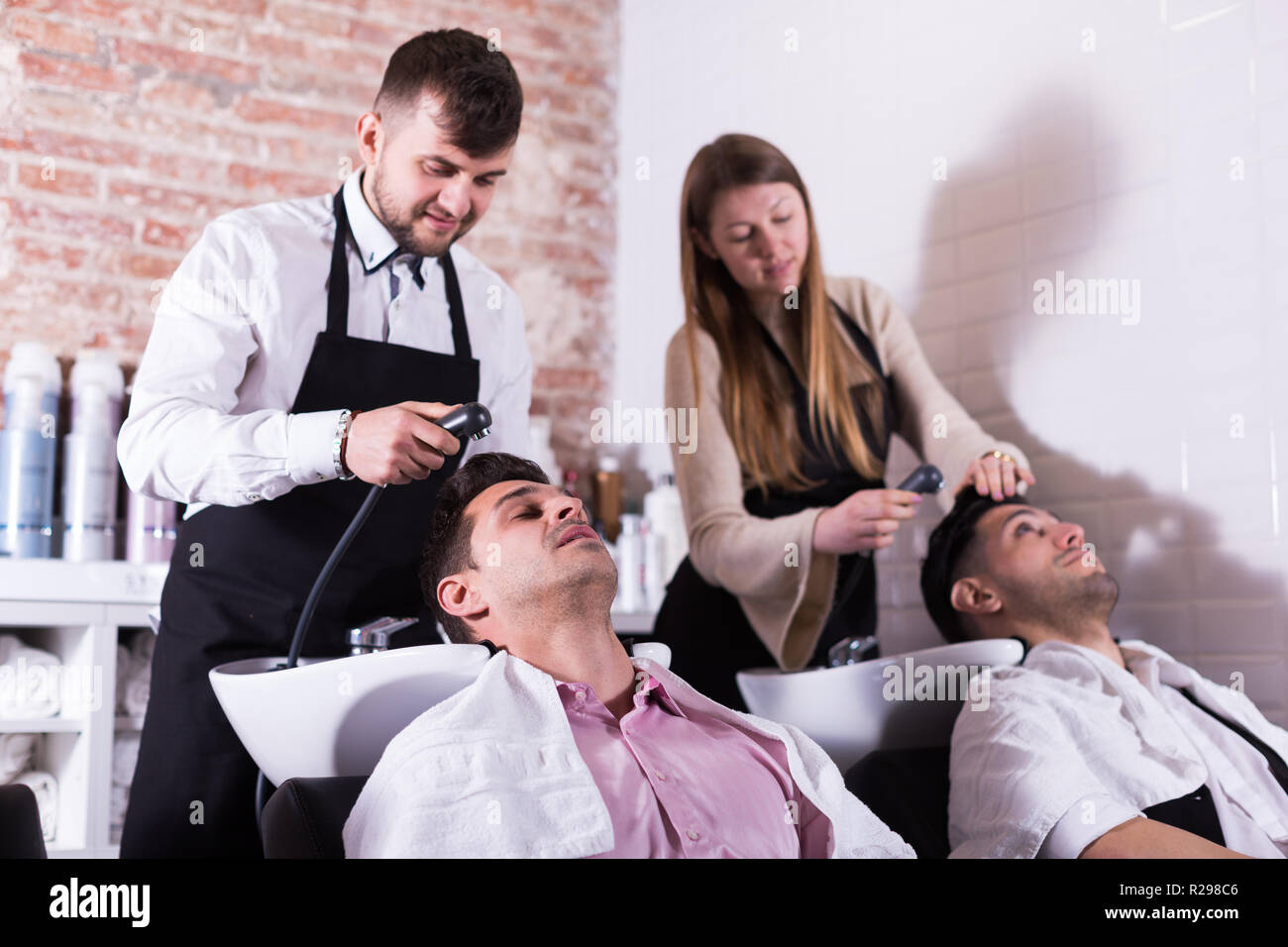 Man And Woman Hairdressers Washing Hair Of Male Clients Of Modern