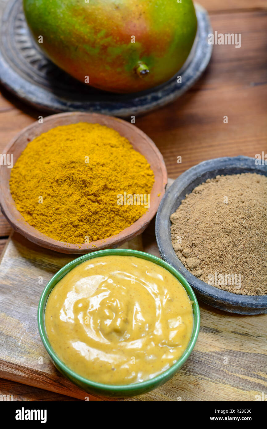 Tasty mango-curry sauce in small bowl ready to eat and bowls with mango and curry powder close- up Stock Photo