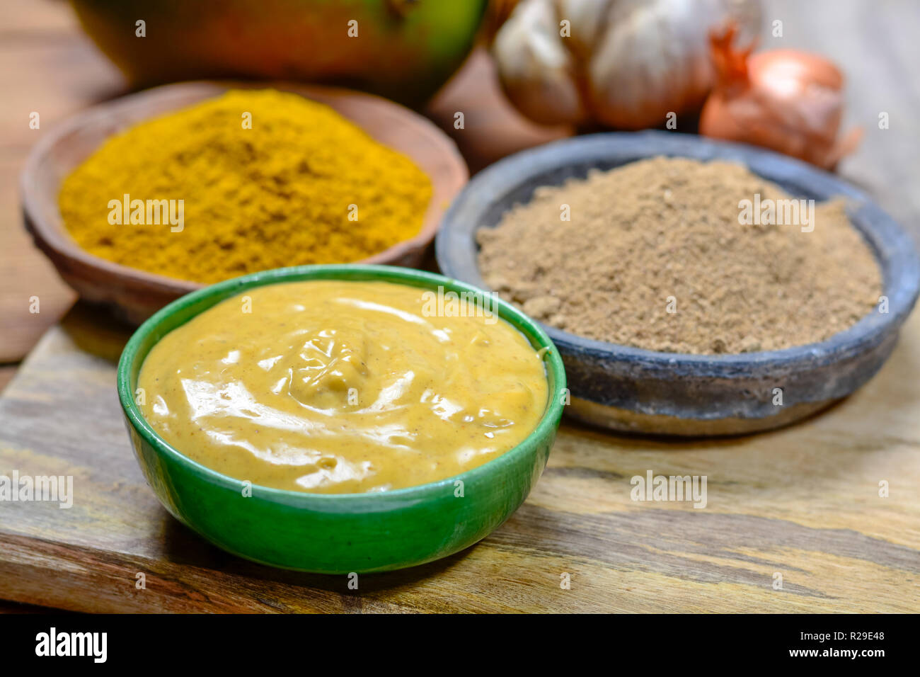 Tasty mango-curry sauce in small bowl ready to eat and bowls with mango and curry powder close- up Stock Photo