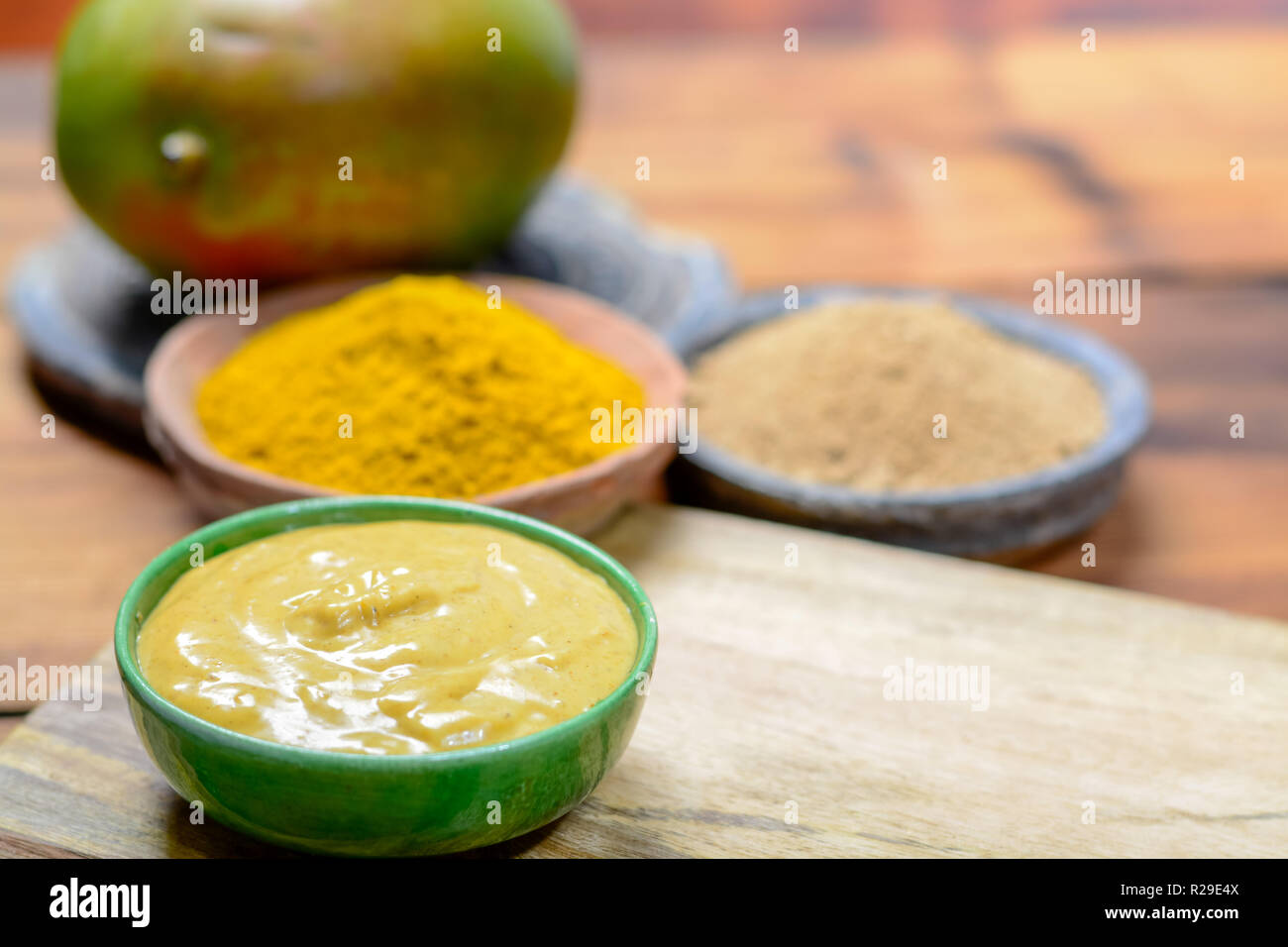 Tasty mango-curry sauce in small bowl ready to eat and bowls with mango and curry powder close- up Stock Photo